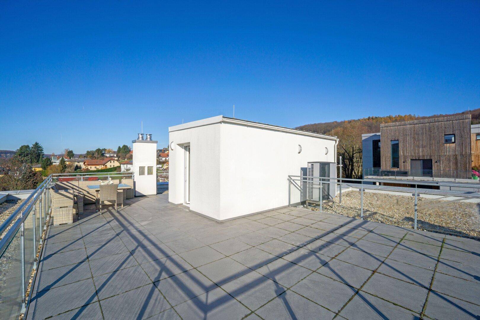 Große Dachterrasse mit Fliesenboden, Glasgeländer und Sitzgelegenheiten.