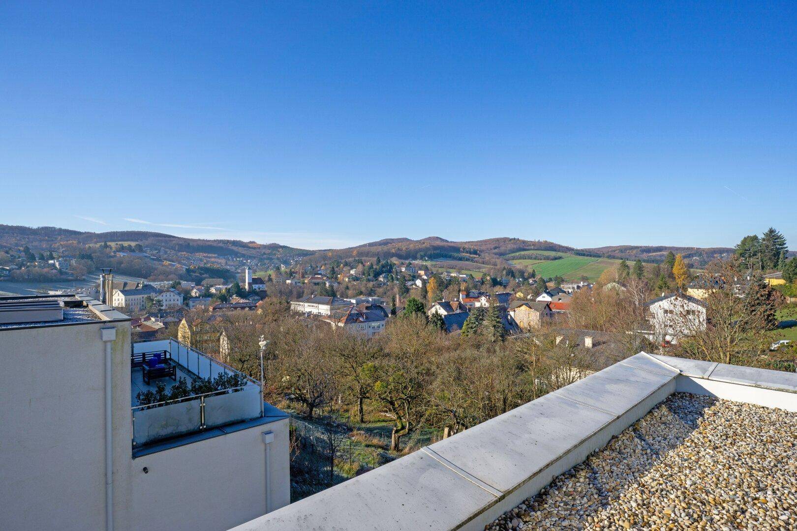 Panoramablick über eine Stadt und die umliegende grüne Hügellandschaft.