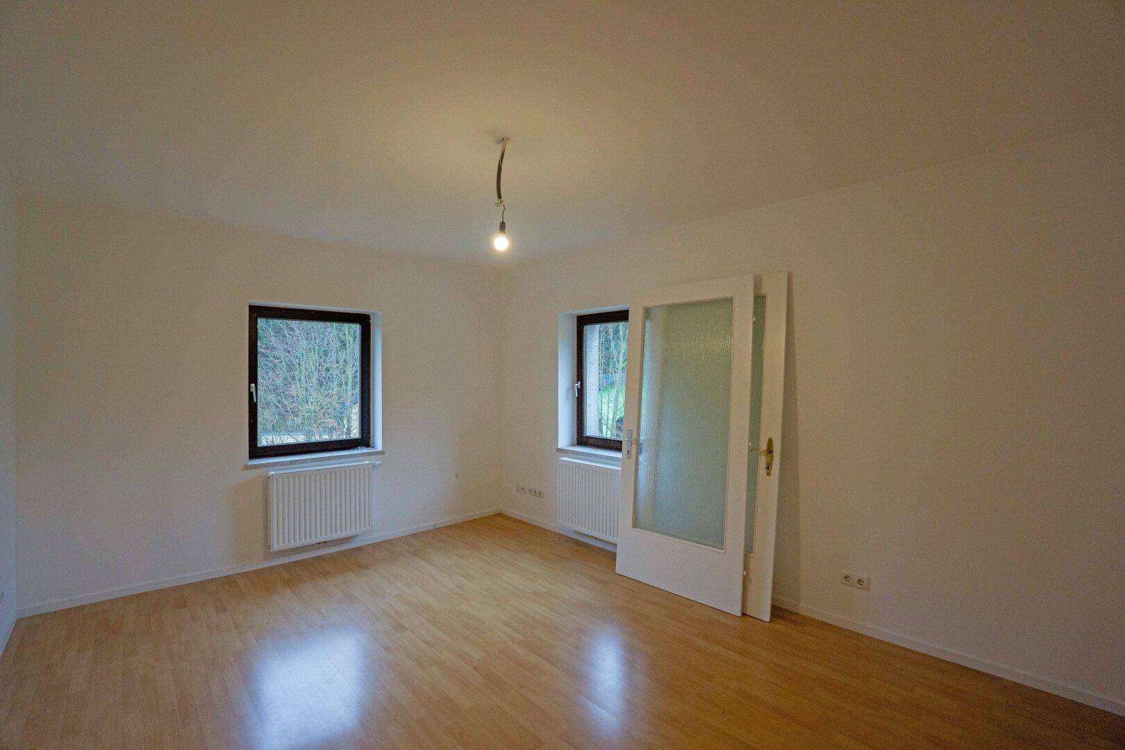 Geräumiges Schlafzimmer mit Laminatboden und zwei Fenstern, die viel Tageslicht hereinlassen.