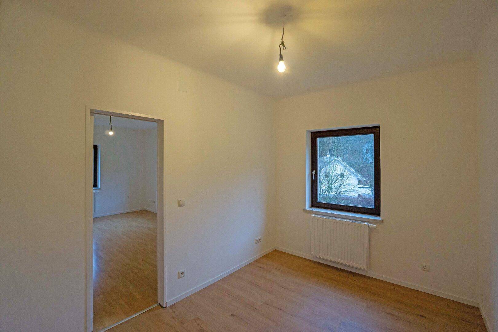 Helles Zimmer mit Laminatboden und Blick auf die umliegende Bebauung und Natur.