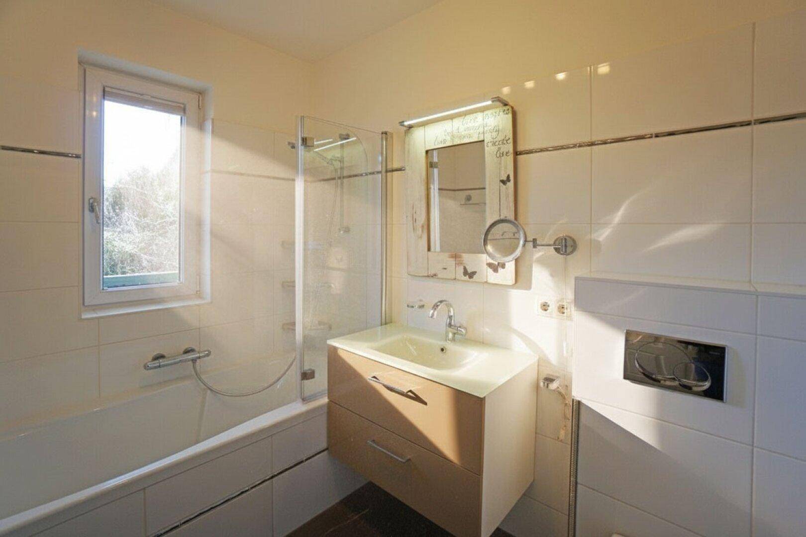 Helles Badezimmer mit Badewanne, Duschbereich, Waschtisch und Fenster für Tageslicht.