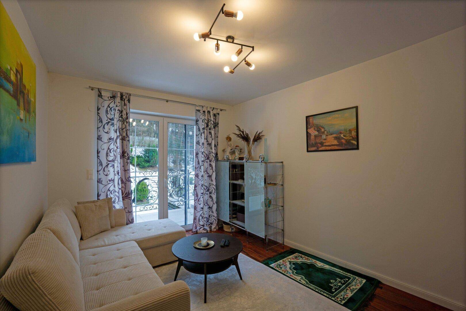 Gemütliches Wohnzimmer mit Sofa, dunklem Holzboden und Zugang zu einem Balkon.