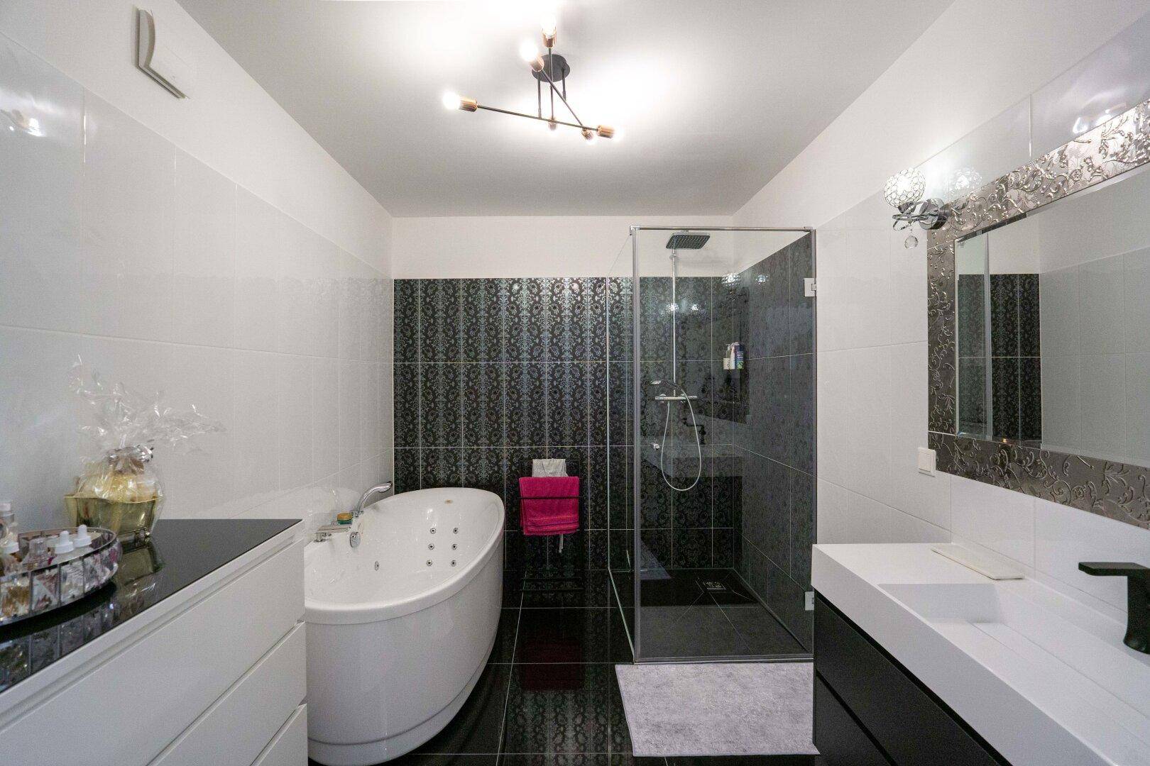 Luxuriöses Badezimmer mit Whirlpool-Badewanne, ebenerdiger Dusche und eleganten schwarzen Fliesen.