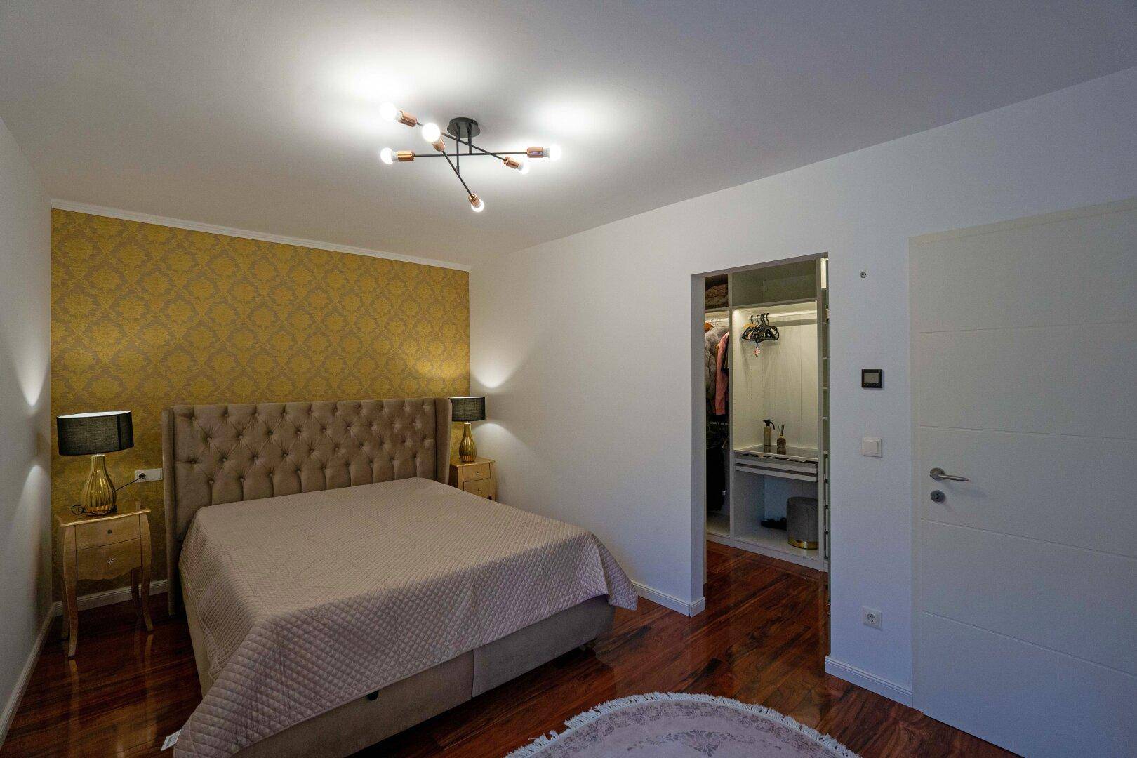 Schlafzimmer mit großem Bett, Holzboden und offenem Zugang zu einem begehbaren Kleiderschrank.