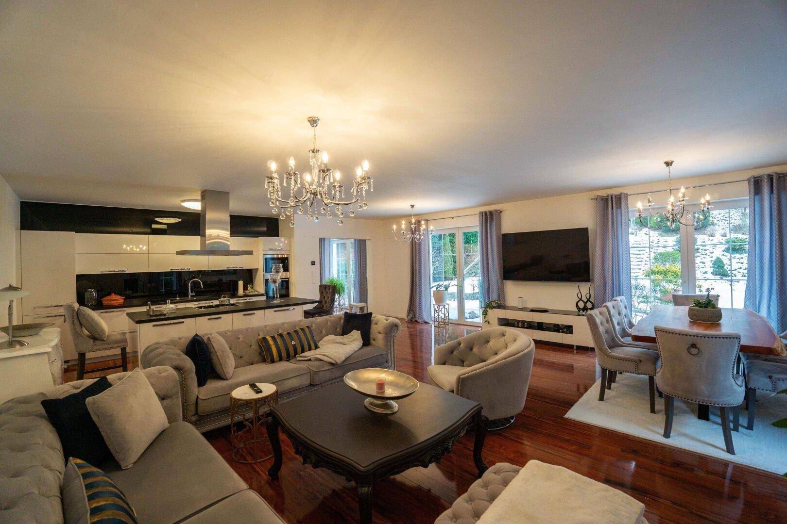 Eleganter offener Wohn-Essbereich mit Kronleuchtern, bequemen Sofas und Holzboden.