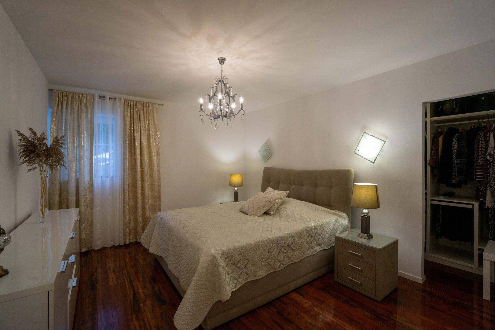 Helles Schlafzimmer mit großem Bett, Holzboden und offenem Zugang zu einem Kleiderschrank.