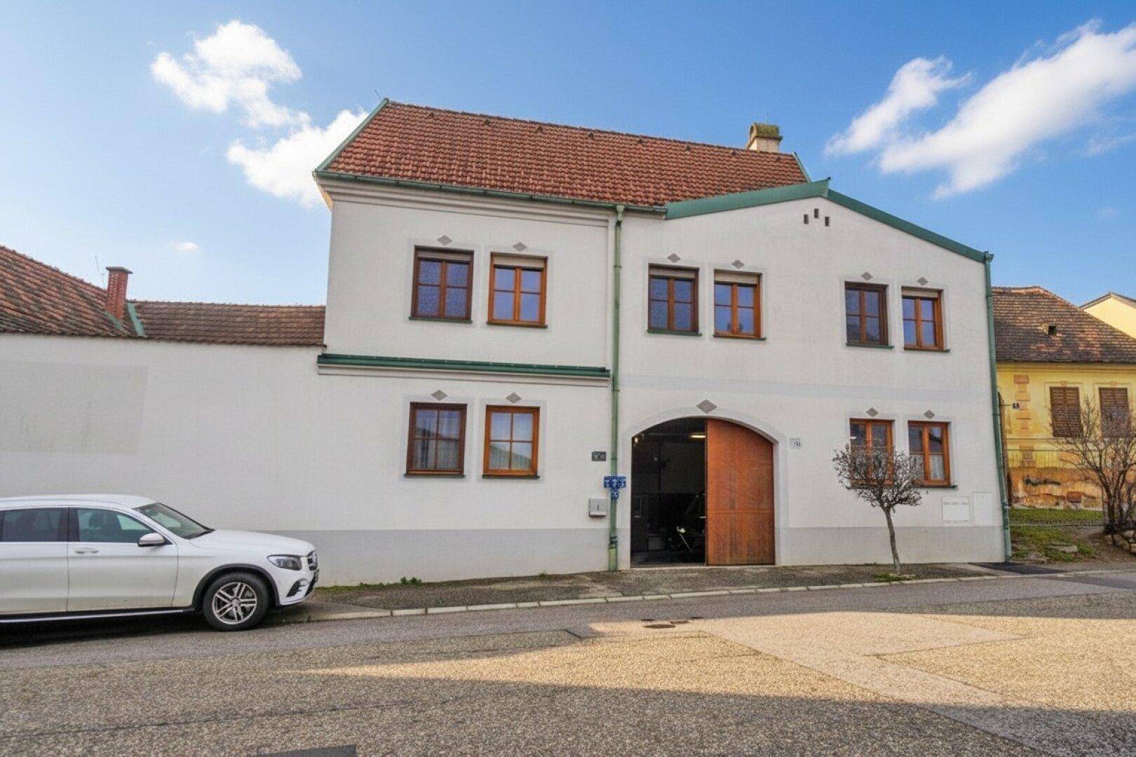 Traditionelles Wohnhaus mit weißer Fassade, roten Ziegeldächern und Holztoren an der Straße.