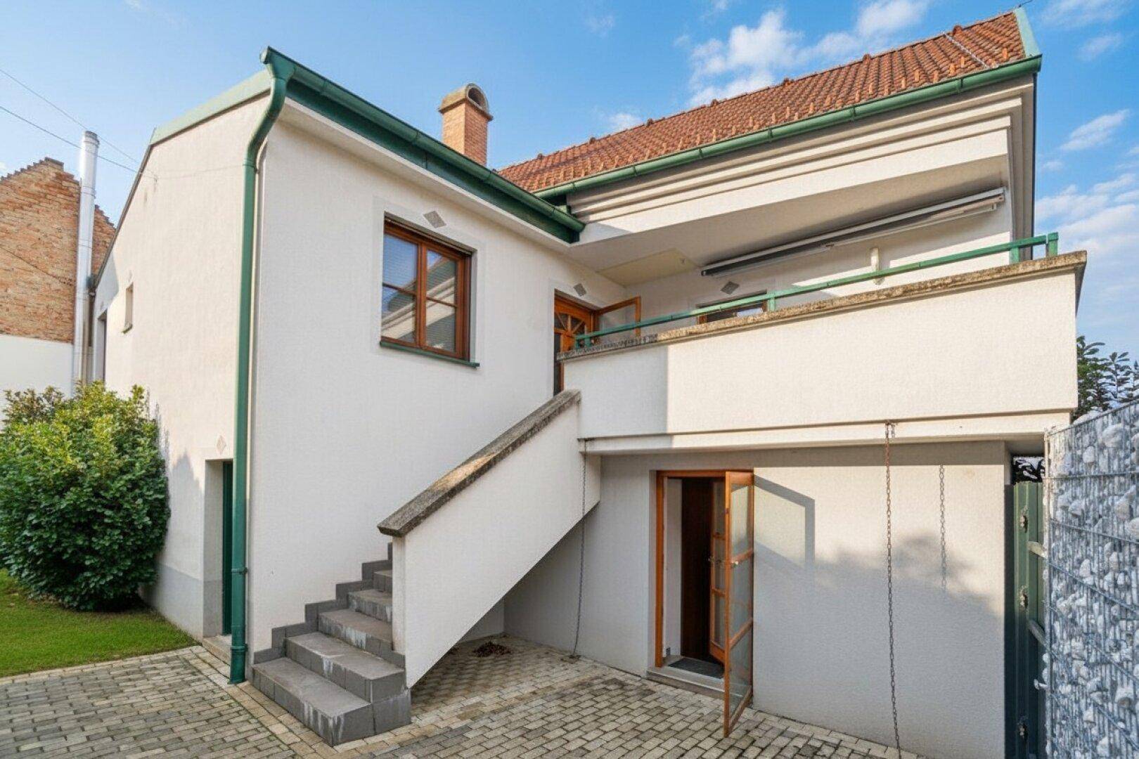 Rückansicht des Hauses mit Außentreppe, Balkon und Zugang zum Gartenbereich.
