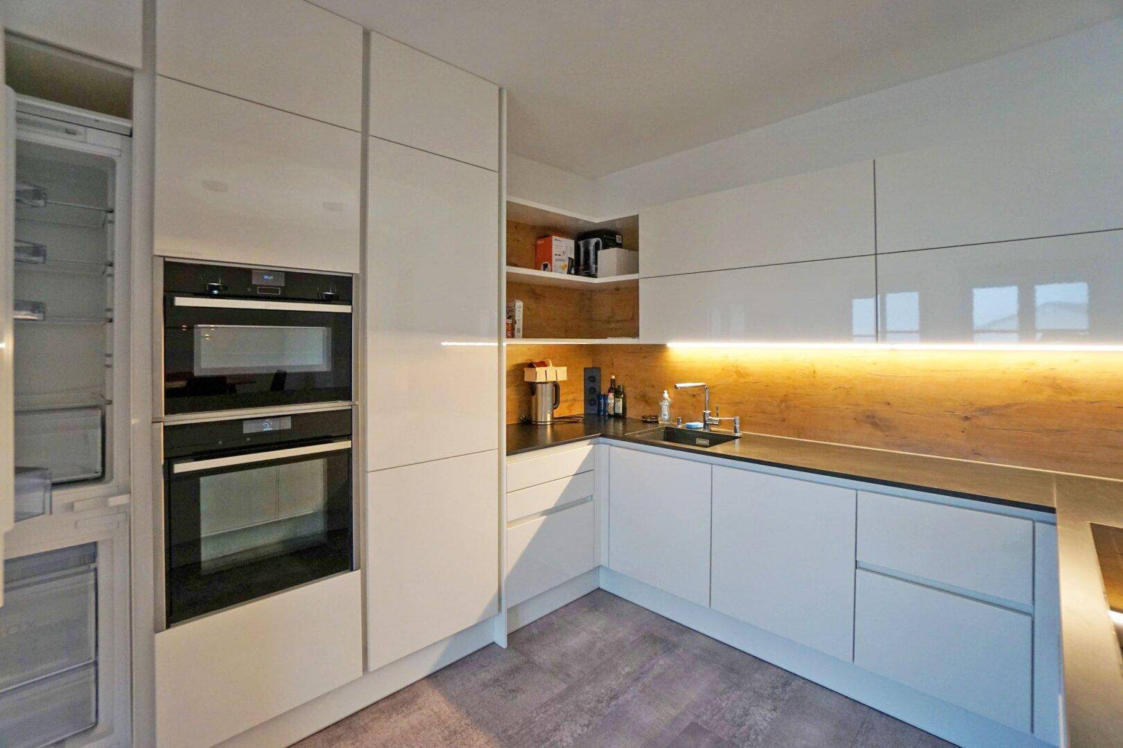 Hochwertige Einbauküche mit weißen Hochglanzfronten, integrierten Geräten und Holzdetails.