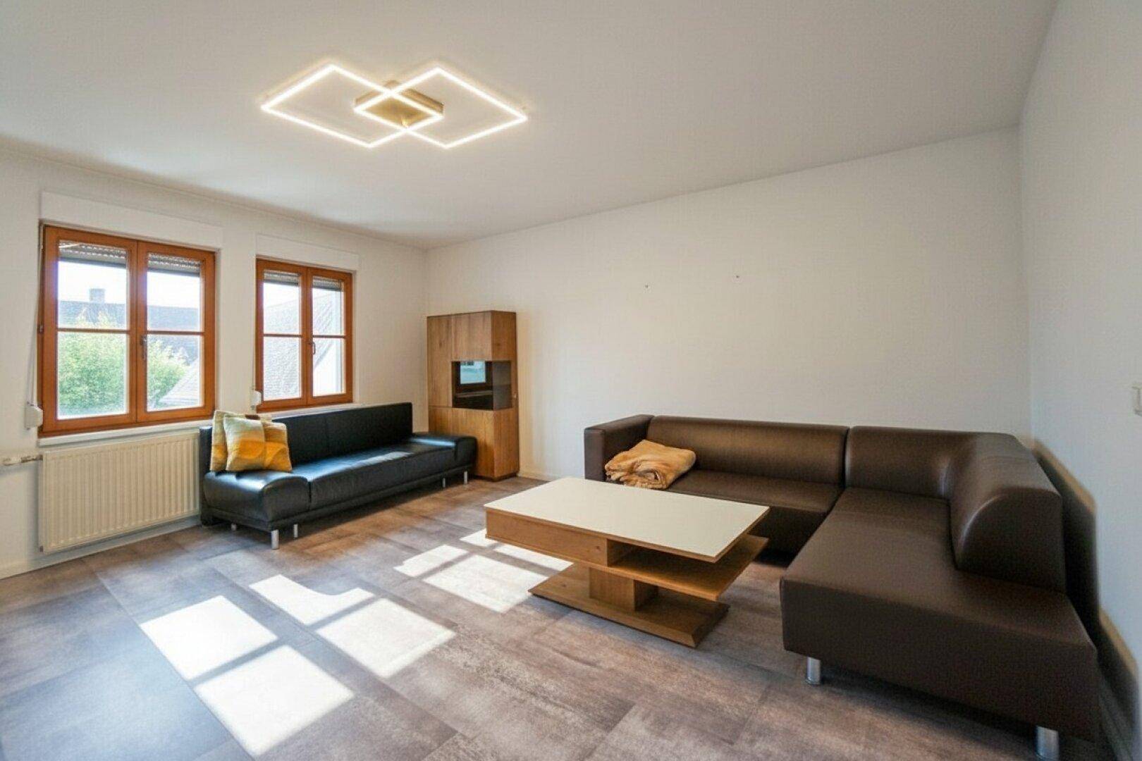 Geräumiges Wohnzimmer mit bequemen Sofas, Couchtisch und großen Fenstern.