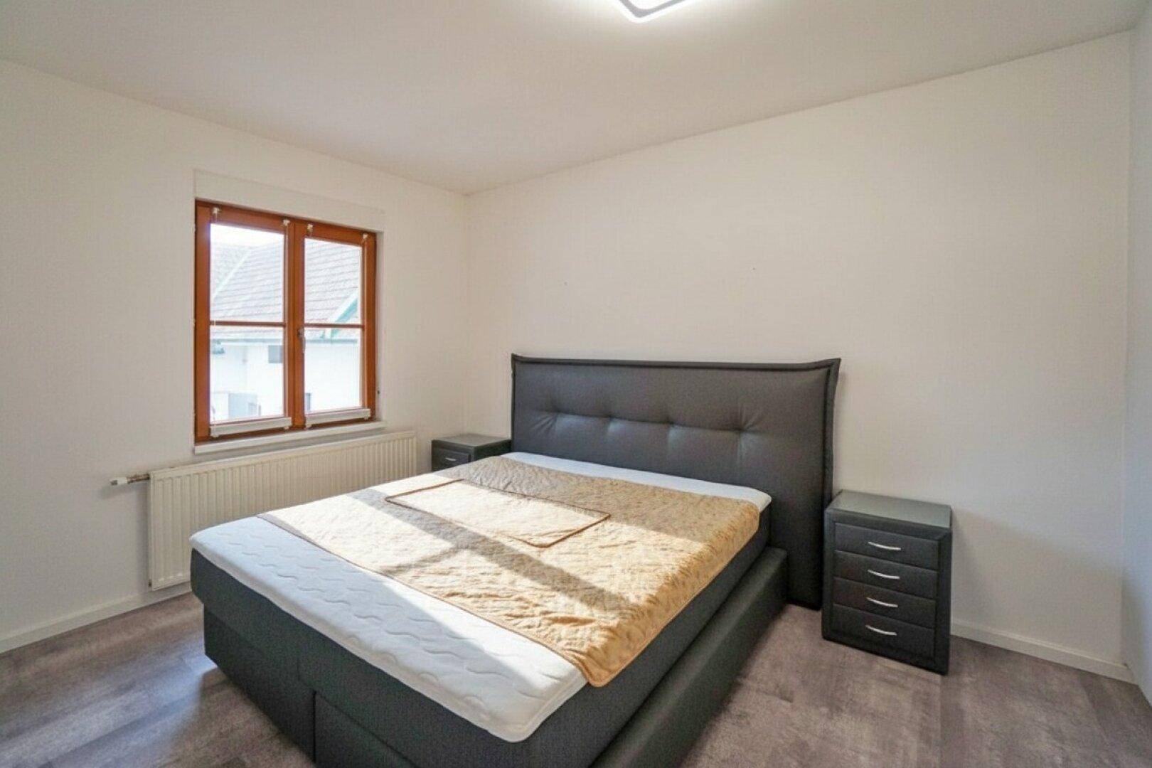 Helles Schlafzimmer mit Doppelbett, Nachttischen und Laminatboden.