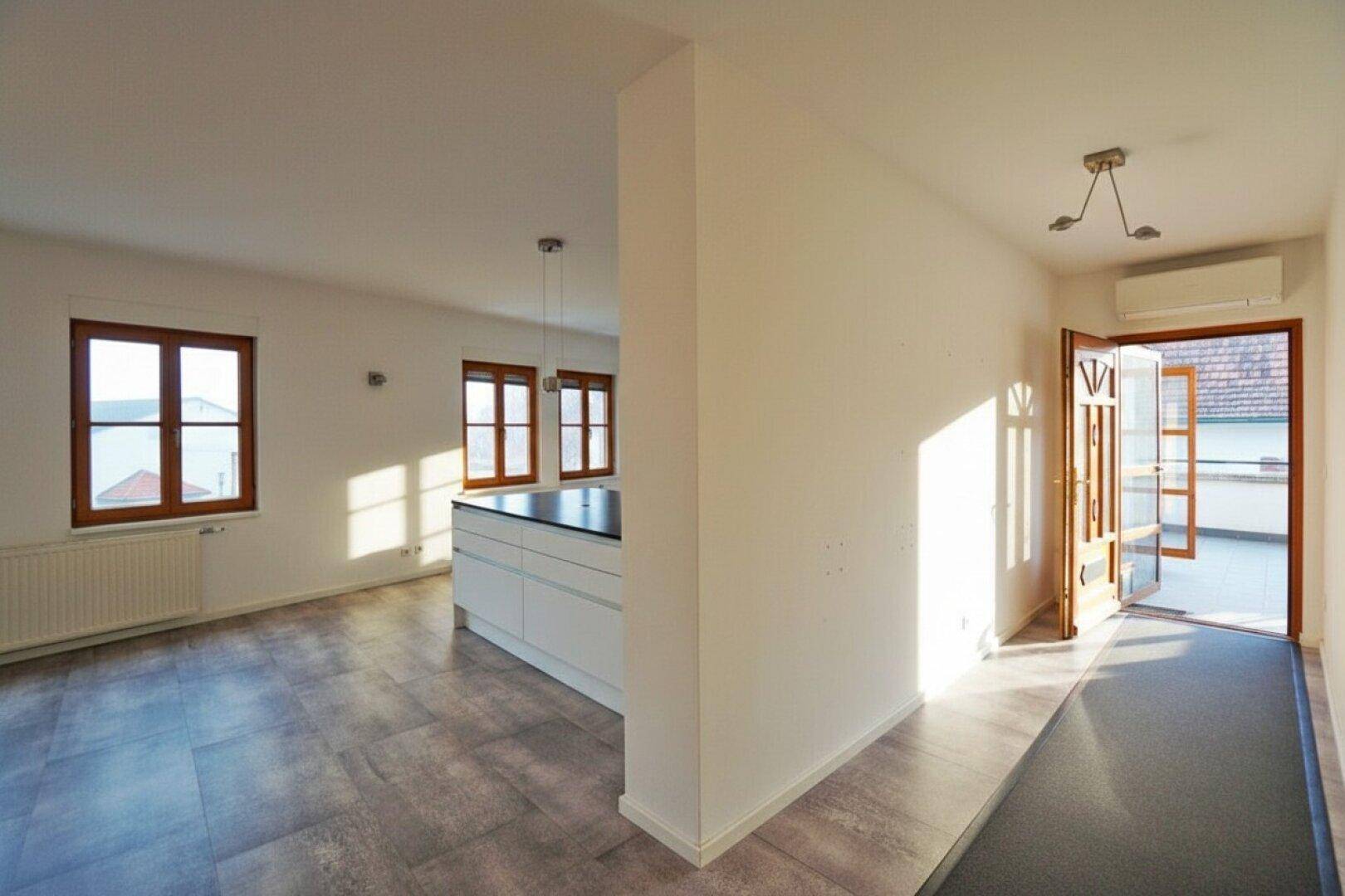 Heller Eingangsbereich mit Zugang zur Terrasse und Blick auf die offene Küche.