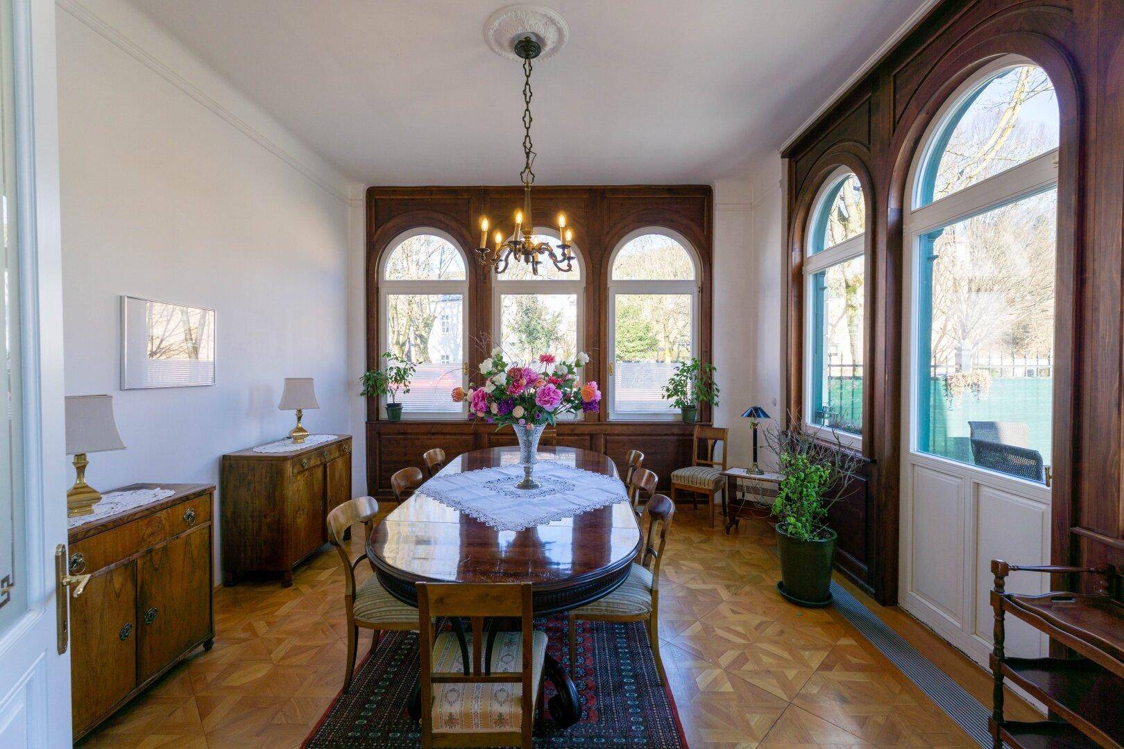 Eleganter Essbereich mit Parkettboden, großem Holztisch und hohen Rundbogenfenstern.