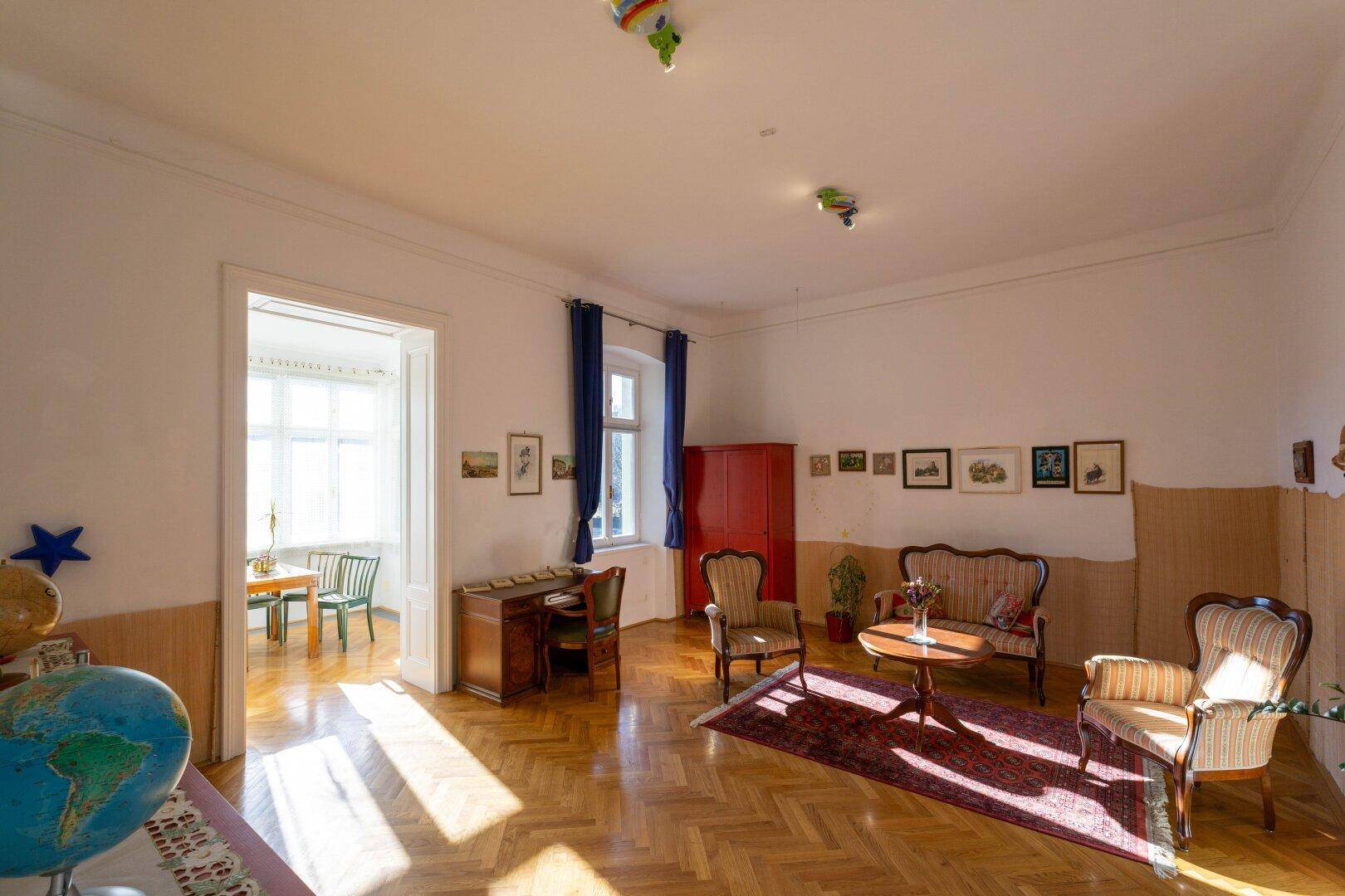 Heller Wohnbereich mit Fischgrätparkett, Vintage-Möbeln und einem Schreibtisch am Fenster.