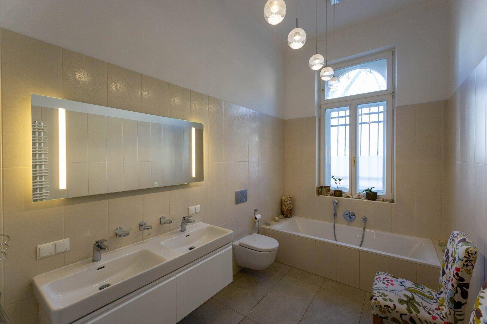 Modernes Badezimmer mit Doppelwaschbecken, Badewanne, Wand-WC und großem Fenster.