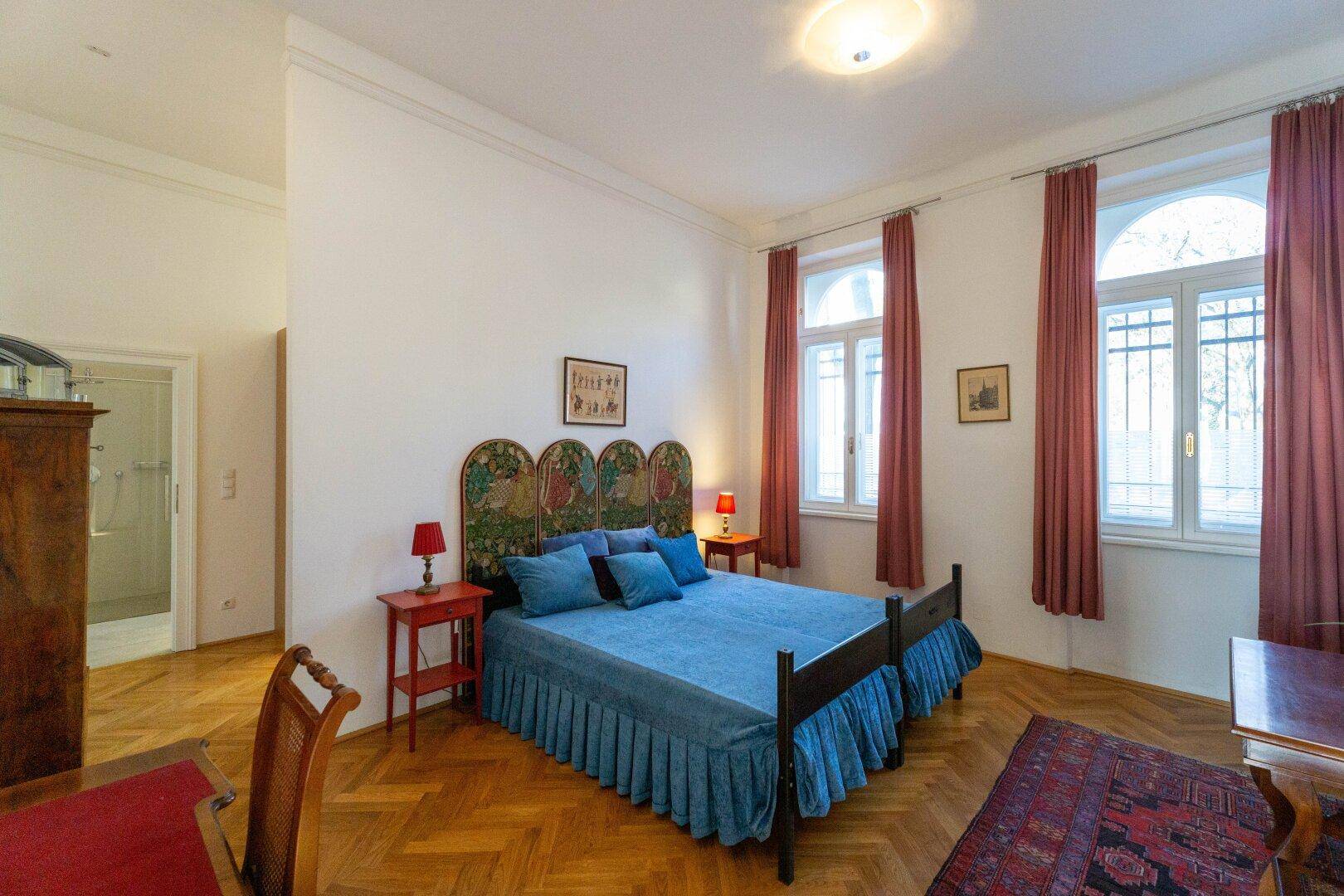 Geräumiges Schlafzimmer mit Parkettboden, großem Bett und hohen, eleganten Rundbogenfenstern.