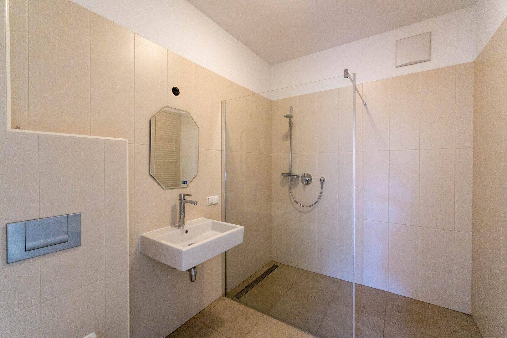 Modernes Badezimmer mit ebenerdiger Dusche, Einzelwaschbecken und hellen Fliesen.