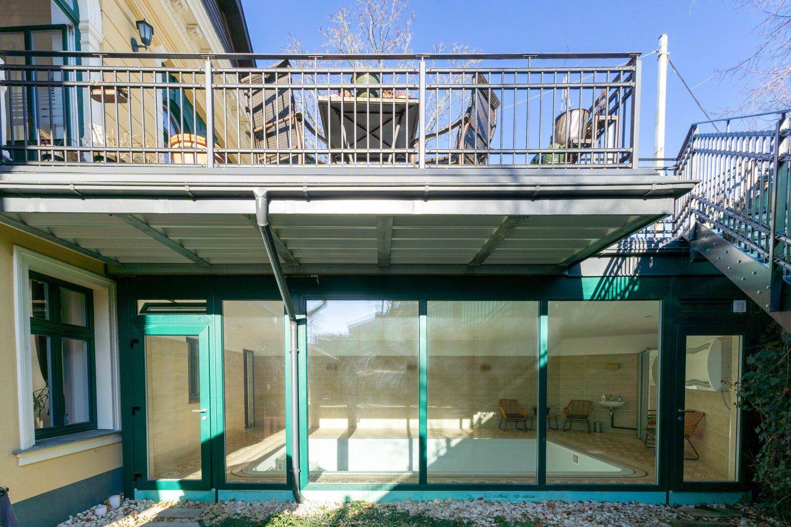 Außenansicht des Gebäudes mit großen Glasfronten, die den Blick auf den Innenpoolbereich freigeben.