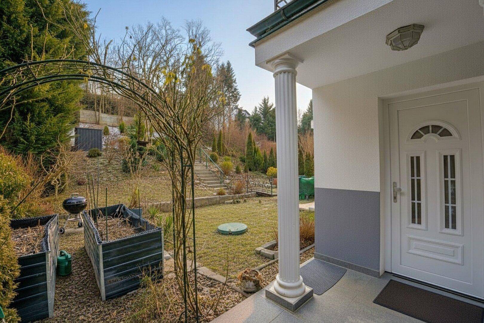 Eingangsbereich mit Zugang zum terrassierten Garten, ausgestattet mit Hochbeeten und Grillplatz.