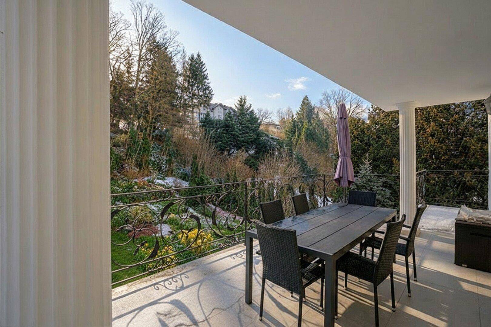 Geräumiger Balkon mit Esstisch und Stühlen, umgeben von üppiger Vegetation und Blick ins Grüne.