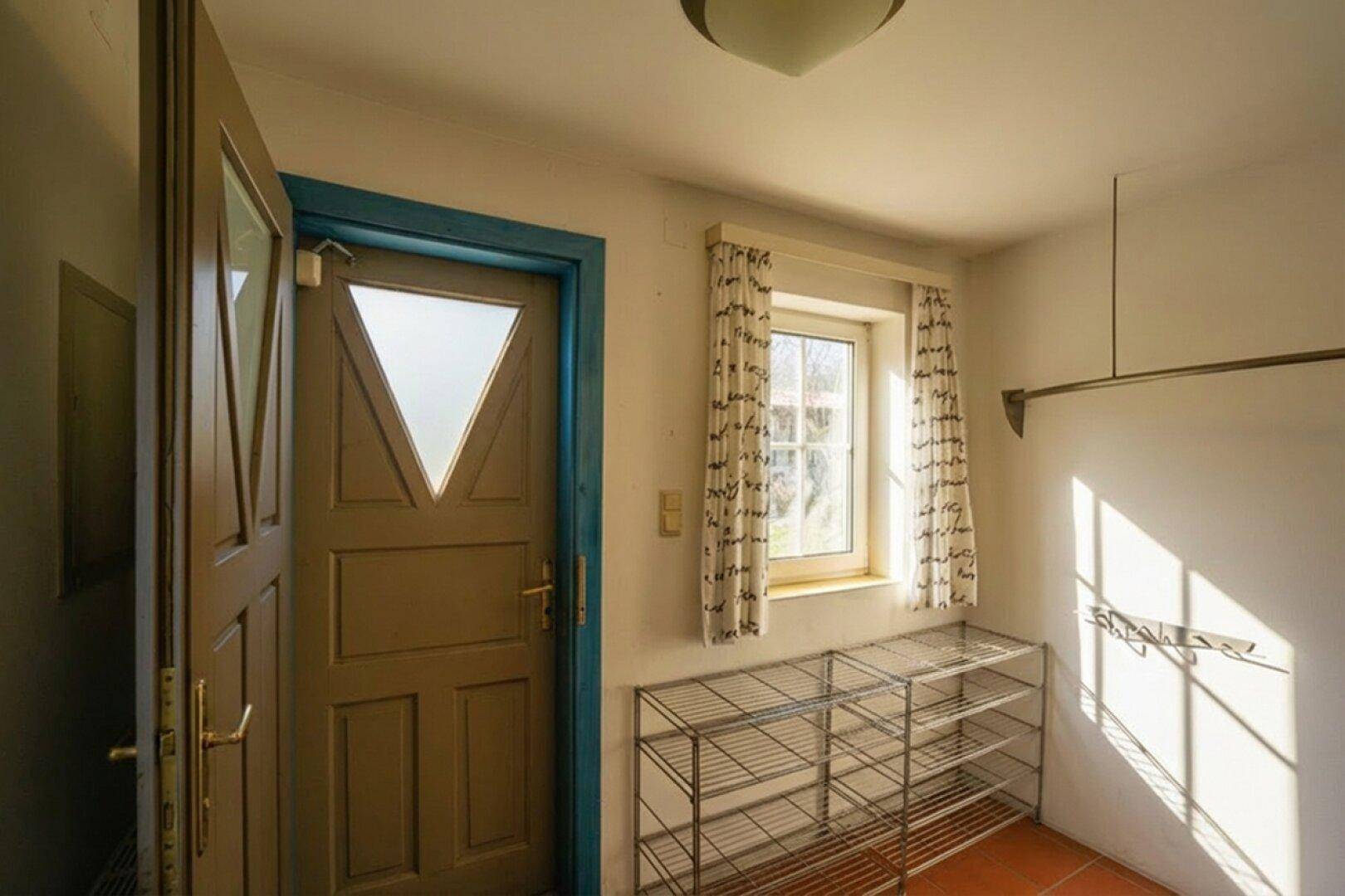 Heller Eingangsbereich mit Fenster, Schuhregal und Terrakottafliesen am Boden.