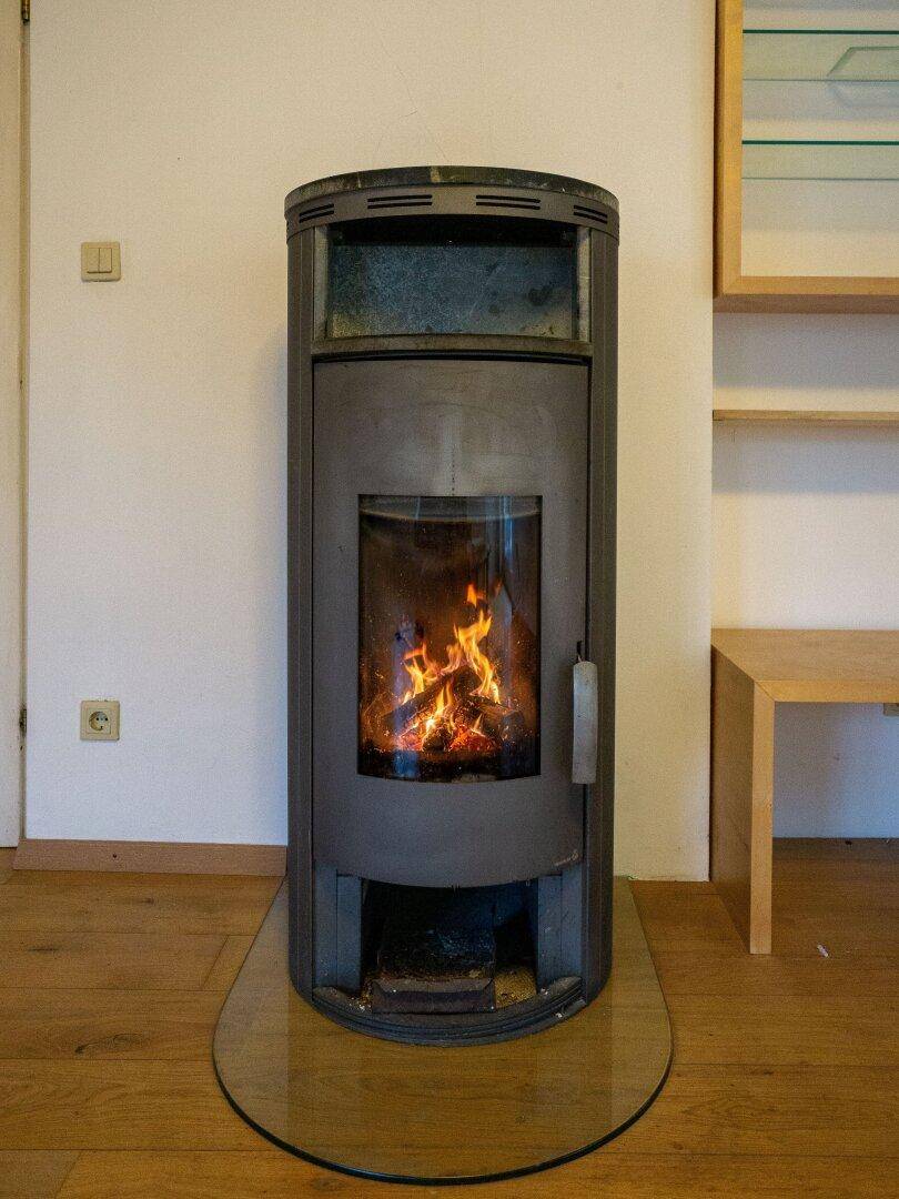 Moderner Kaminofen mit Glasfront auf einer Glasplatte im Wohnbereich.