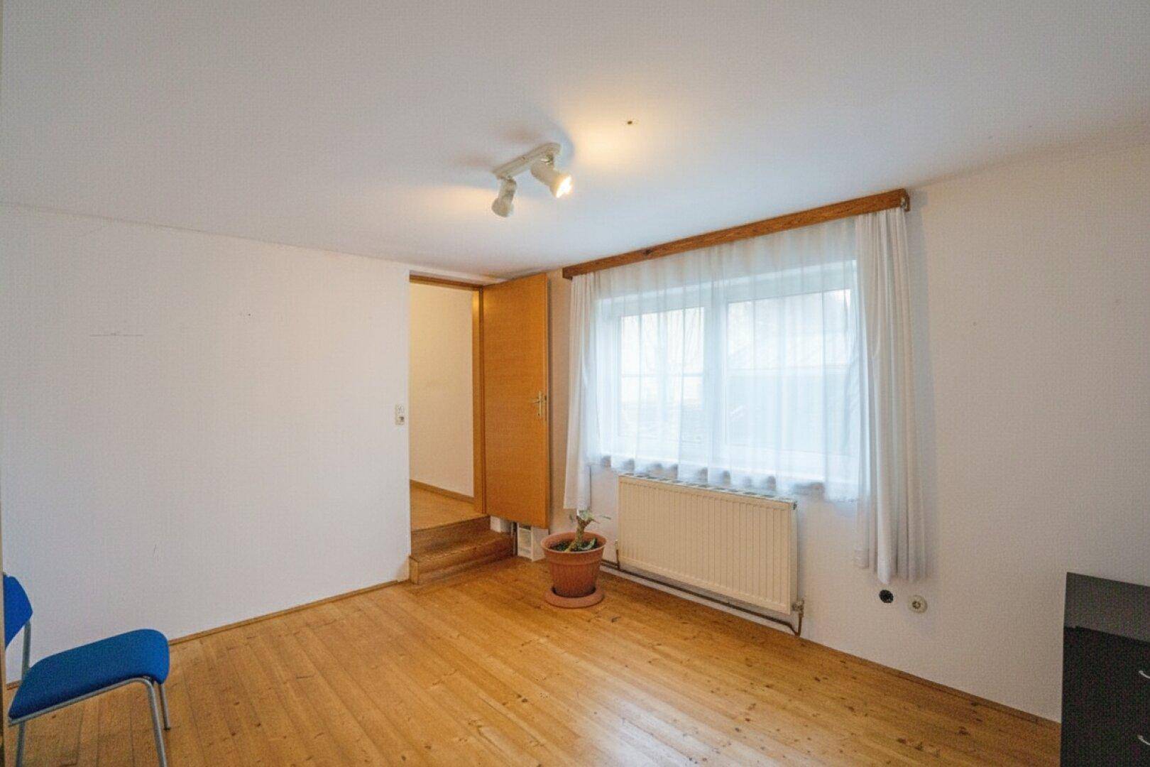 Helles Zimmer mit Holzboden, großem Fenster und Heizkörper, bereit zur individuellen Gestaltung.
