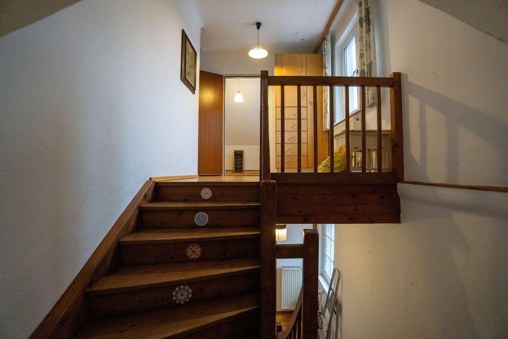 Holztreppe mit Geländer führt in die obere Etage, mit natürlichem Lichteinfall.