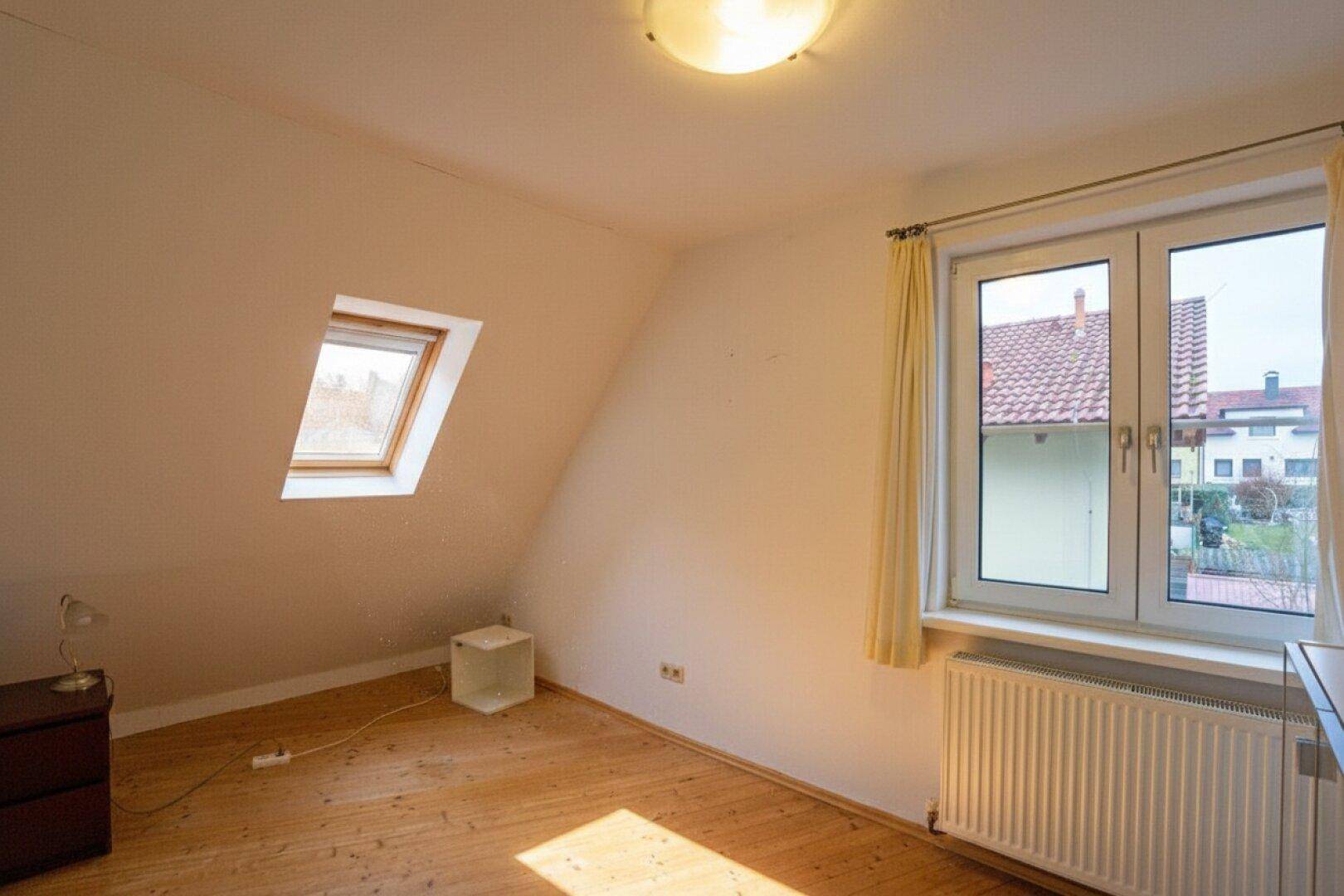 Helles Schlafzimmer mit Holzboden, Fenster und Dachfenster, bietet viel Tageslicht.