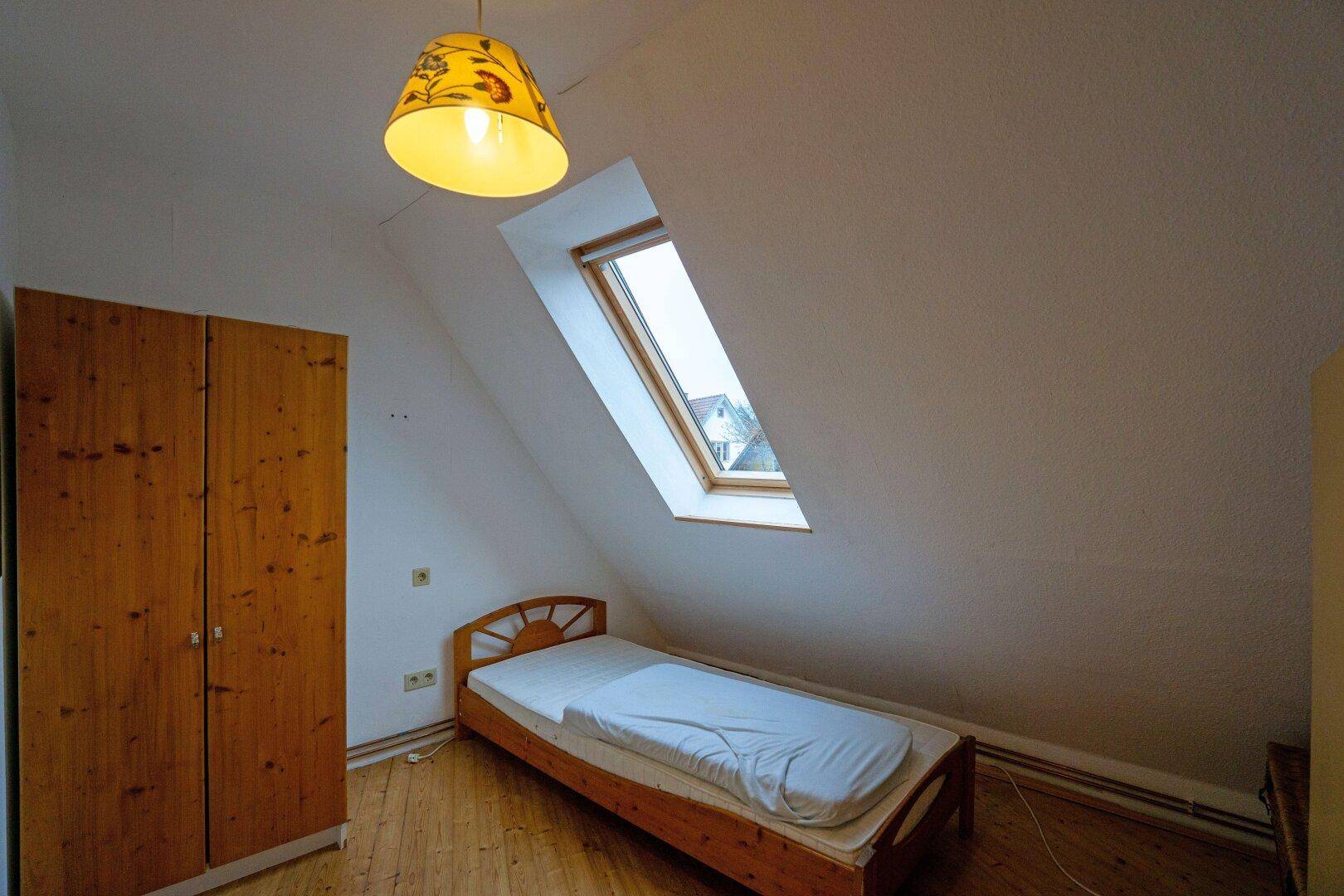 Schlafzimmer mit Holzboden, Einzelbett und Dachfenster unter der schrägen Decke.
