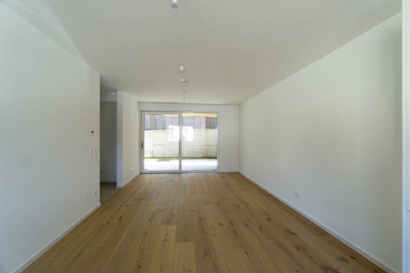 Heller Wohnraum mit Holzboden und großer Glasschiebetür, die zu einem kleinen Außenbereich führt.