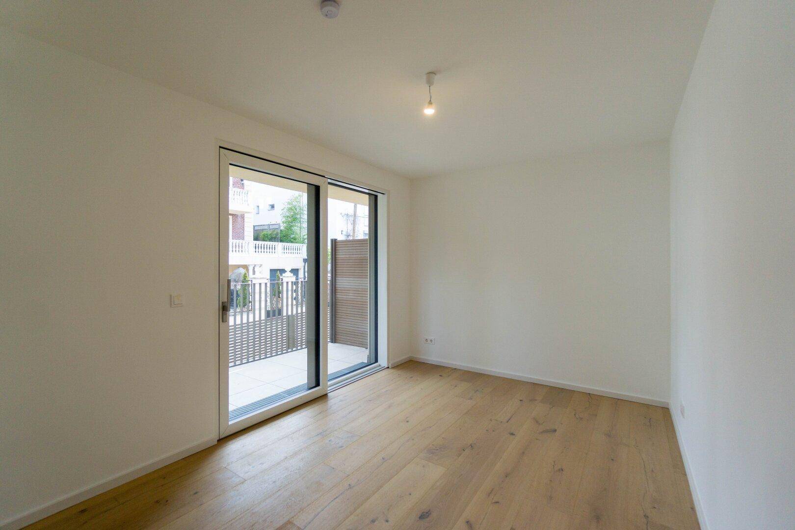 Lichtdurchfluteter Raum mit Holzboden und großer Schiebetür, die zu einem Balkon führt.