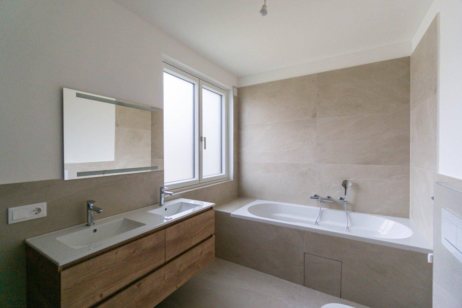 Modernes Badezimmer mit Doppelwaschbecken, Badewanne, großen Fliesen und Fenster.