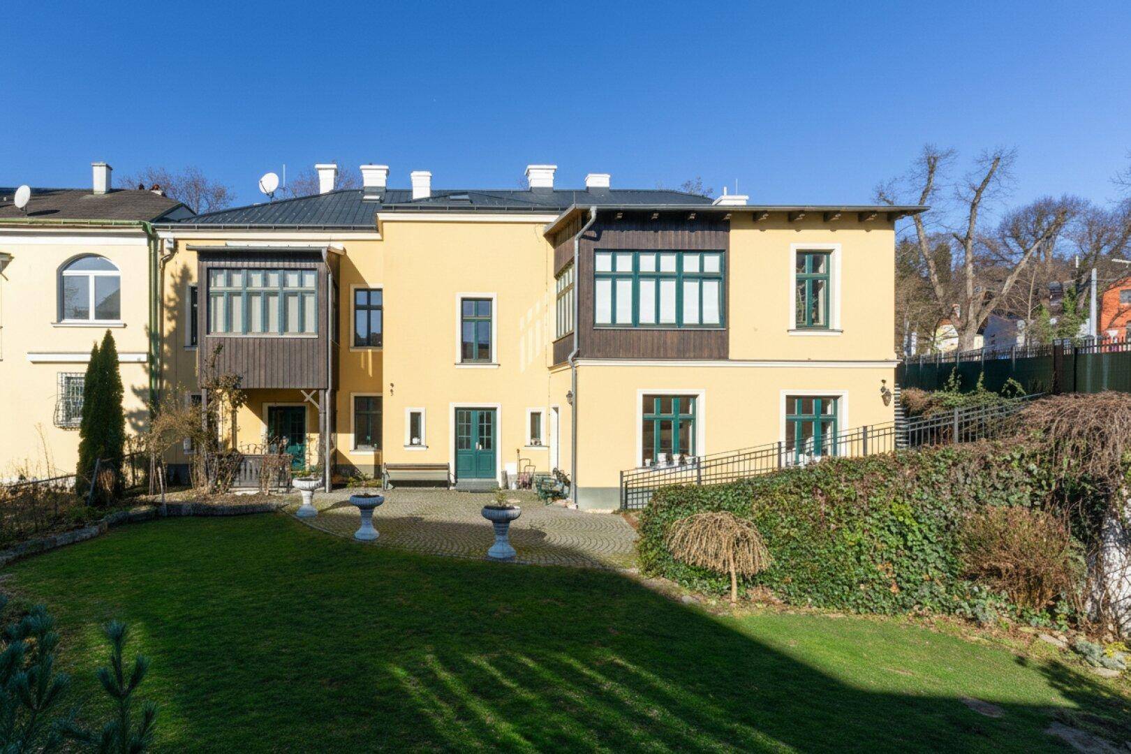 Rückansicht des Gebäudes mit gepflegtem Garten, Rasenfläche und barrierefreiem Zugang über eine Rampe.