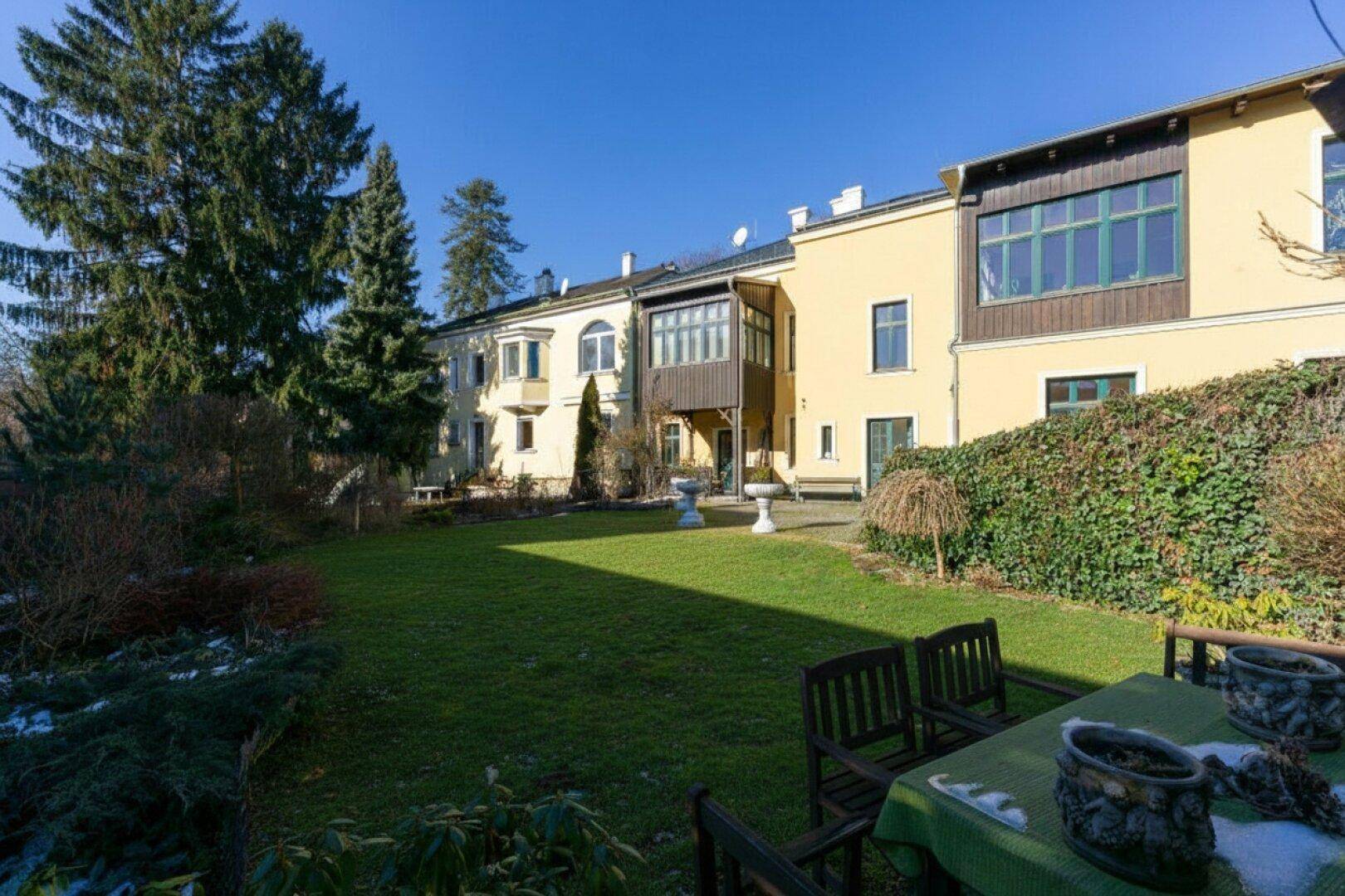 Weitläufiger Garten mit großer Rasenfläche, altem Baumbestand und Sitzgelegenheiten im Freien.