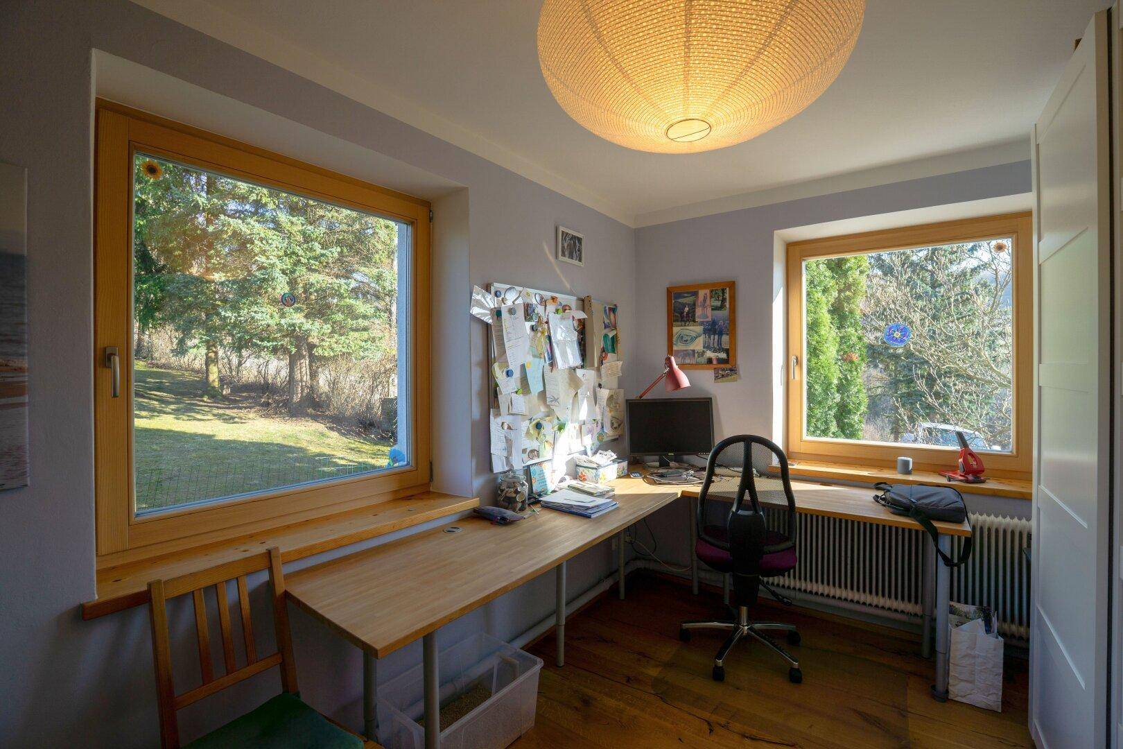 Helles Arbeitszimmer mit Holzfenstern, Schreibtisch und Blick auf den grünen Garten.