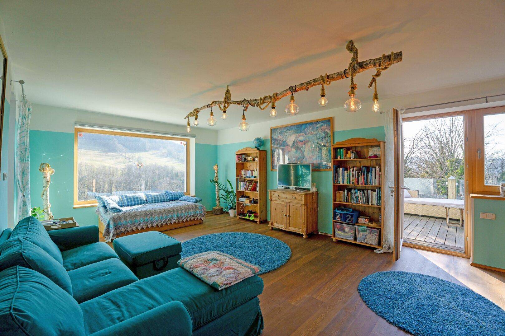 Geräumiges Wohnzimmer mit blauer Couch, Holzregalen und Zugang zu einem Balkon.