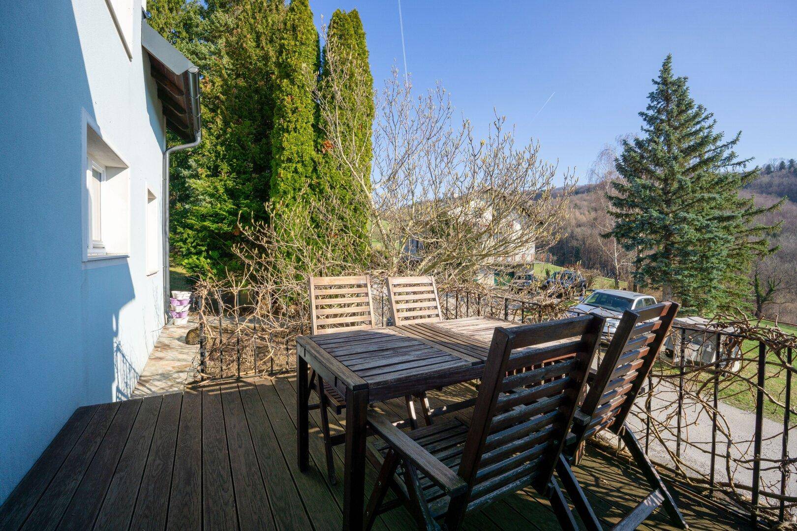 Sonniger Holzbalkon mit rustikalen Gartenmöbeln und weitem Blick in die grüne Landschaft.