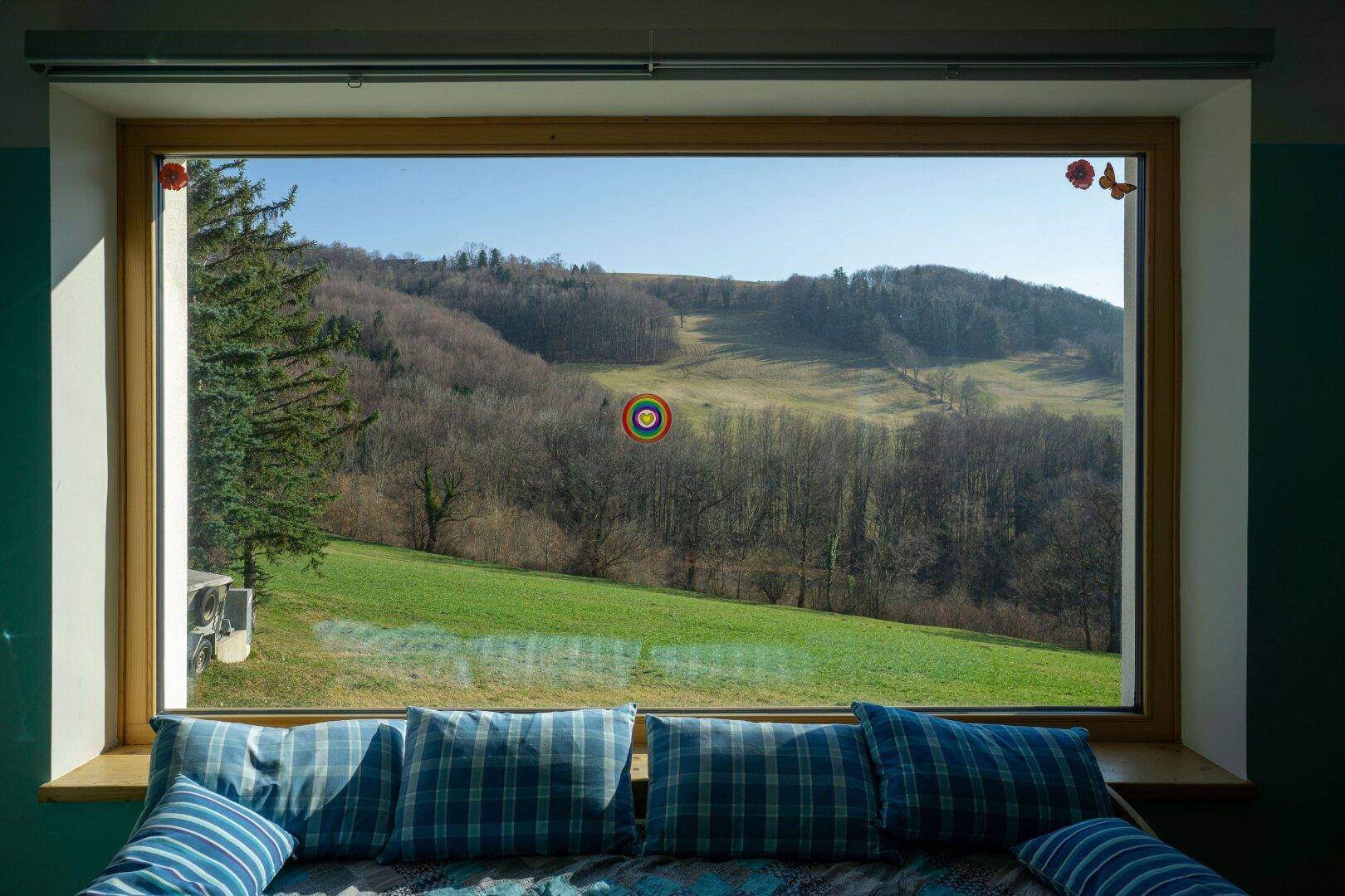 Große Fensterfront im Wohnzimmer bietet einen weiten Blick auf die grüne Hügellandschaft.