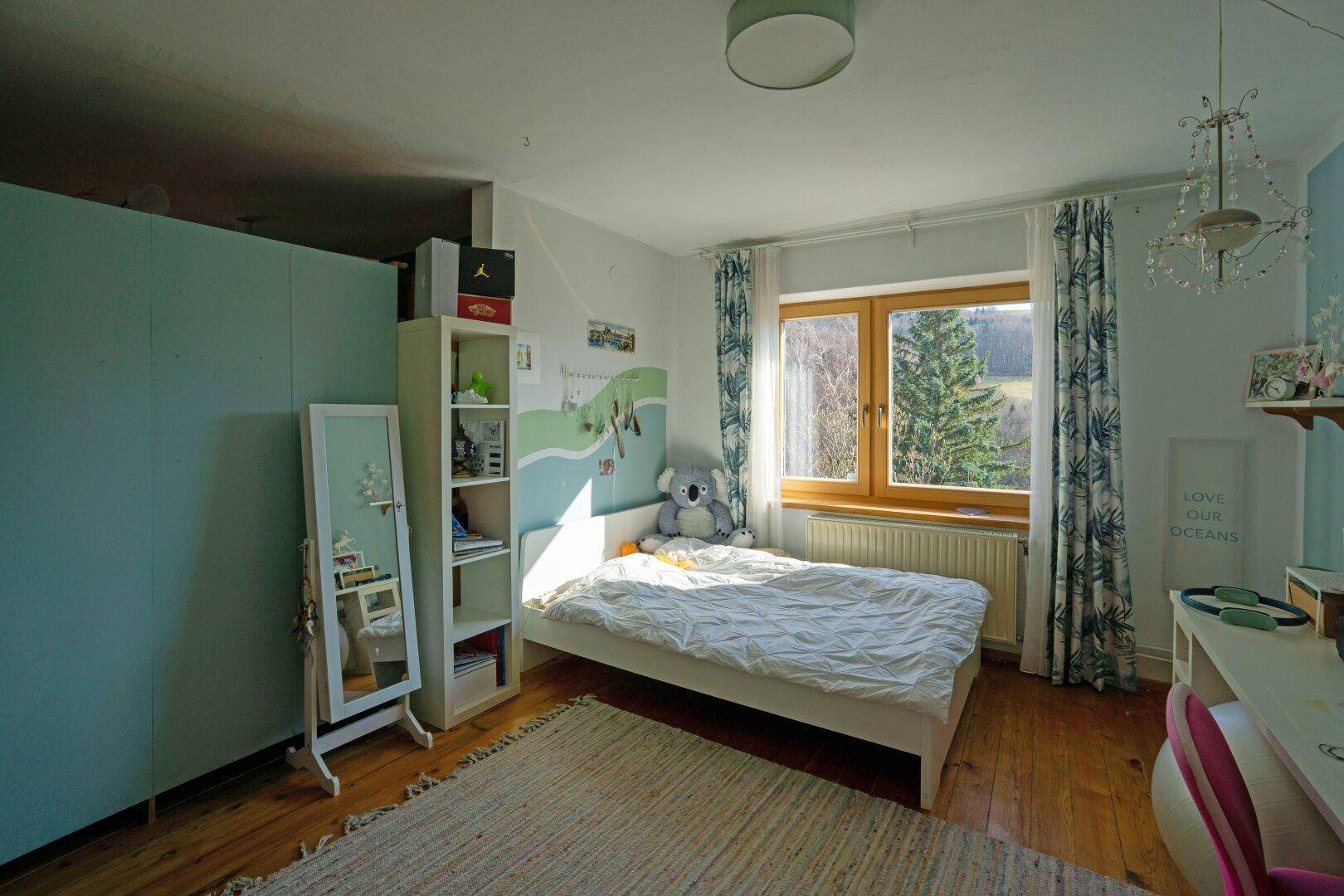 Kinderzimmer mit Holzboden, Einzelbett und Fensterblick auf die umliegende Natur.