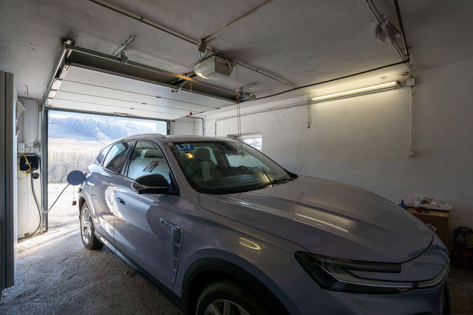 Garage mit einem Elektrofahrzeug an der Ladestation und offenem Garagentor.