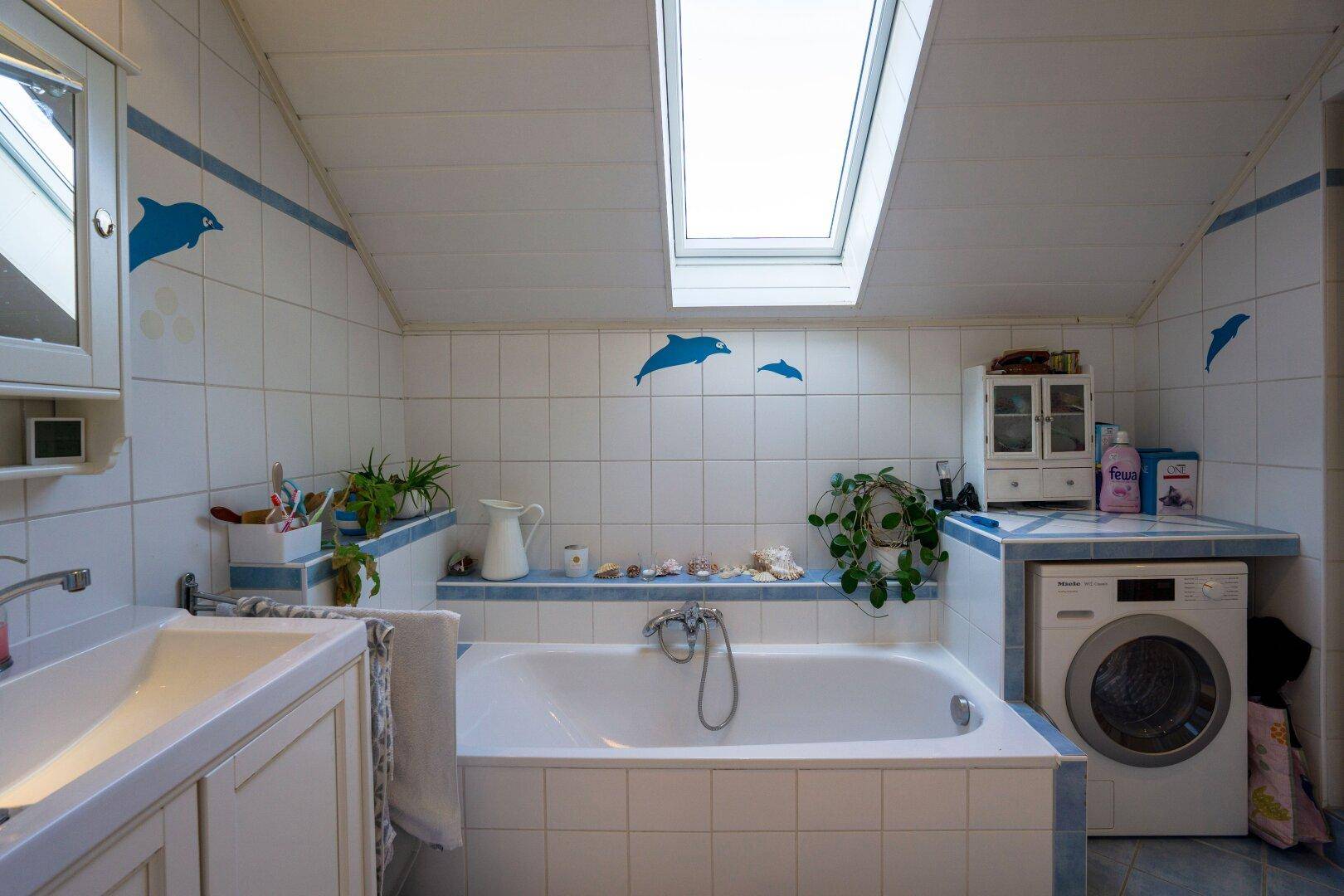 Gefliestes Badezimmer mit Badewanne, Waschmaschine und Dachfenster für natürliches Licht.