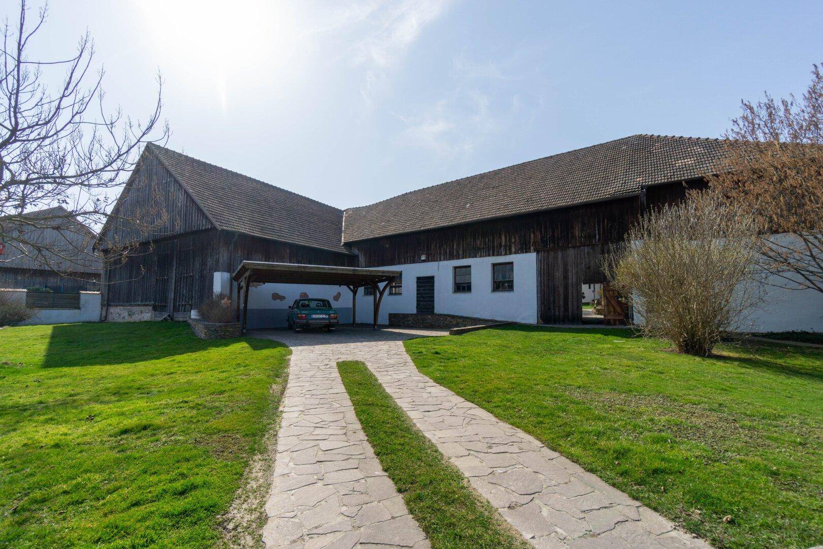 Zufahrt zum Anwesen mit Carport und großen Scheunengebäuden im ländlichen Stil.