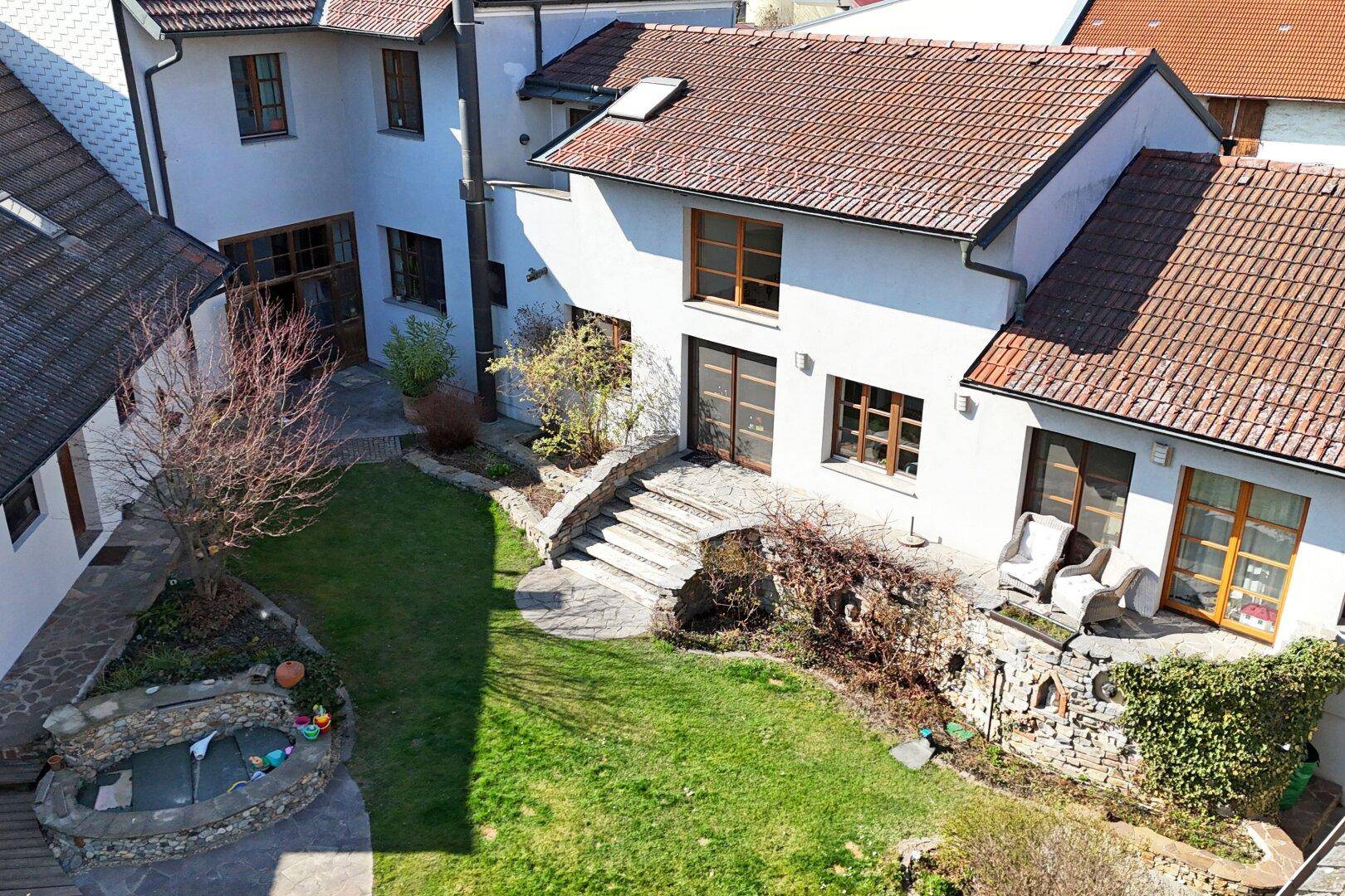 Vogelperspektive des Wohnhauses mit gepflegtem Garten, Steintreppen und Außensitzbereich.