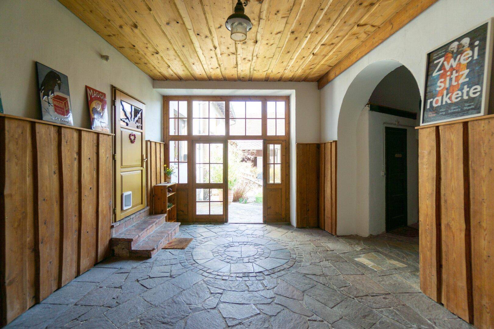 Geräumiger Eingangsbereich mit Holzwänden, Holzbalkendecke und Steinboden mit Mosaik.