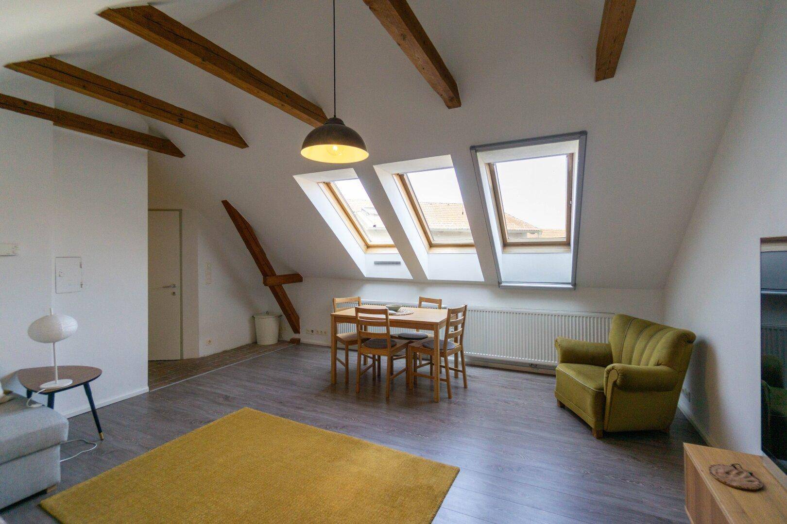 Gemütlicher Wohnbereich im Dachgeschoss mit Holzbalken, Dachfenstern und Essplatz.