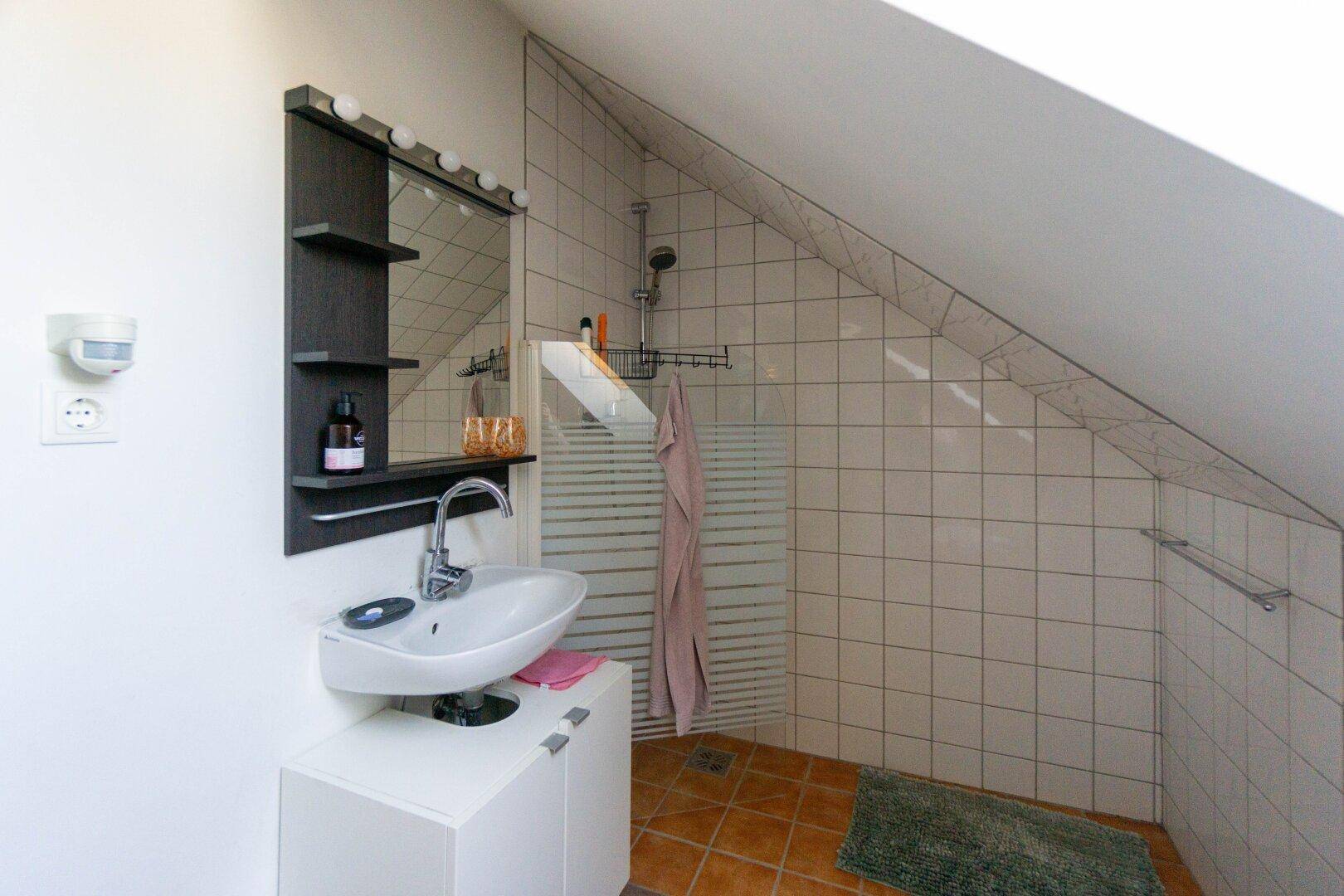 Badezimmer im Dachgeschoss mit Schrägwand, Dusche und weißen Fliesen.