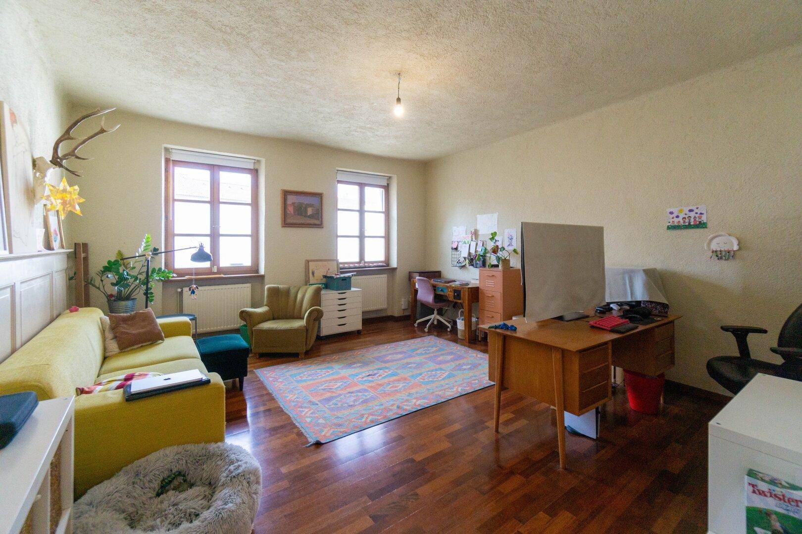 Geräumiges Arbeitszimmer mit Holzboden, zwei Fenstern und traditioneller Einrichtung.