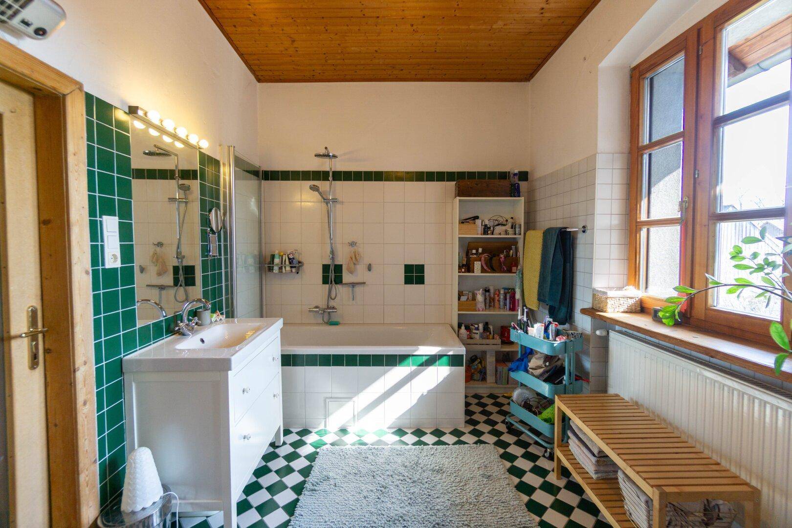 Badezimmer mit grünen und weißen Fliesen, Badewanne und Fenster.