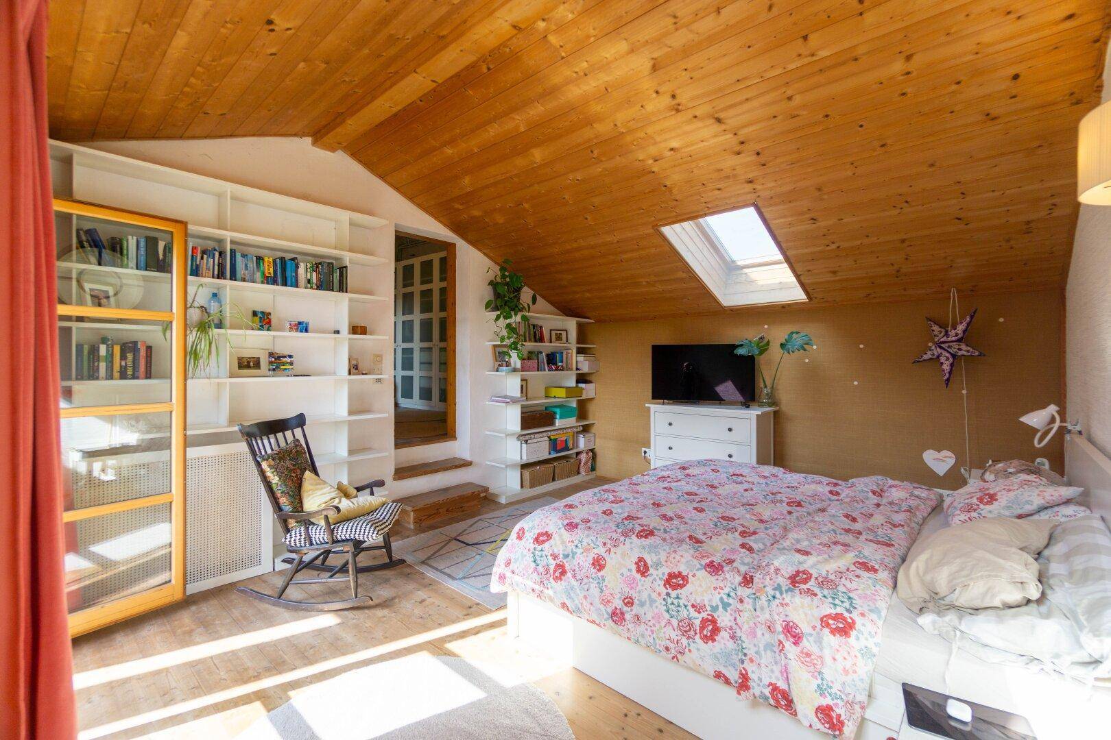 Schlafzimmer im Dachgeschoss mit Holzbalkendecke, Dachfenster und eingebauten Regalen.